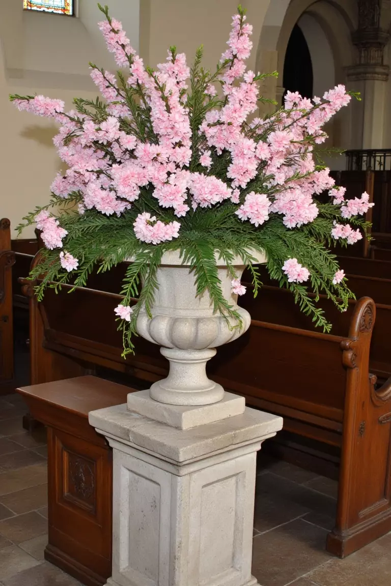 Overflowing Urn With Flowers A photo of a large stone urn filled with blush-pink flowers at the top of a church aisle