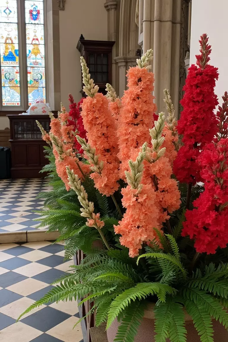 Rich Reds and Soft Greenery A photo of red and peach blooms in urns with fluffy ferns lining a church altar area