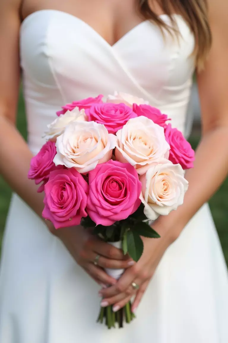 Roses in Various Hues A photo of a bride holding a rose bouquet featuring shades of pale pink, bubble gum, and fuchsia