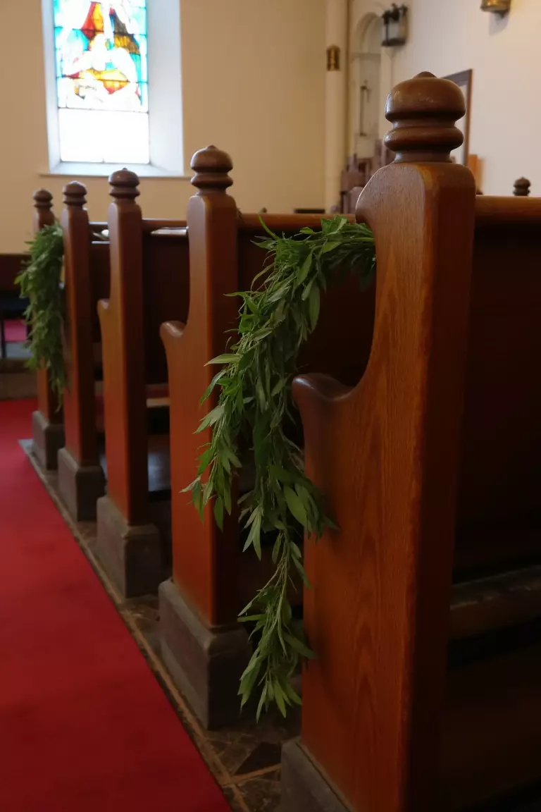 Go All Greenery A photo of church pews decorated with simple strands of greenery draped along the sides