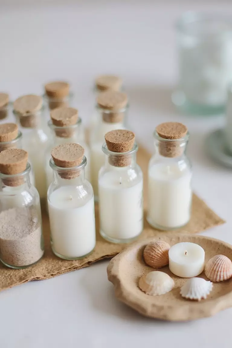 Give Out Beachy Wedding Favors A professional photo, similar to a photo in a wedding magazine, of neatly arranged wedding favors including tiny glass bottles with sand, miniature seashells, and beach-themed candles.