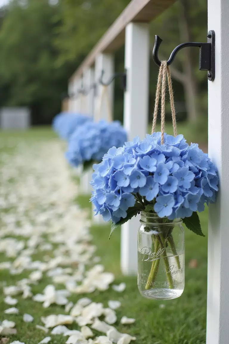 Hydrangea Aisle Decorations A professional photo, similar to a photo in a wedding magazine, of a wedding aisle lined with hanging mason jars filled with blue hydrangeas on shepherd's hooks.