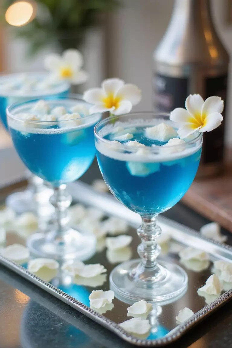 Blue Signature Cocktails A professional photo, similar to a photo in a wedding magazine, of crystal glasses containing vibrant blue signature cocktails garnished with white flower petals on a mirrored bar top.