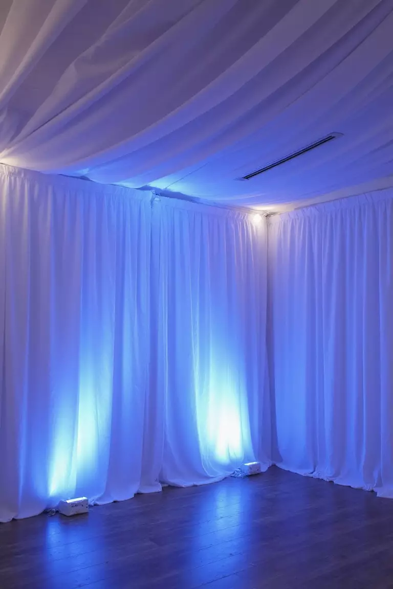 White Chiffon Drapery With Blue Uplighting A professional photo, similar to a photo in a wedding magazine, of flowing white chiffon drapery illuminated by soft blue uplighting creating an ethereal ballroom atmosphere.