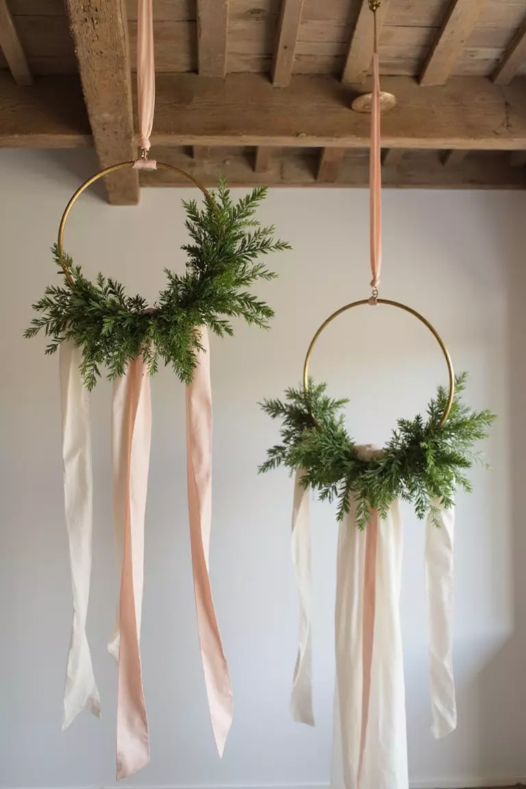 Suspended Hoop Garlands With Trailing Ribbons A professional photo, similar to a photo in a wedding magazine, of golden hoops suspended from ceiling beams with greenery and flowing silk ribbons in blush and ivory.