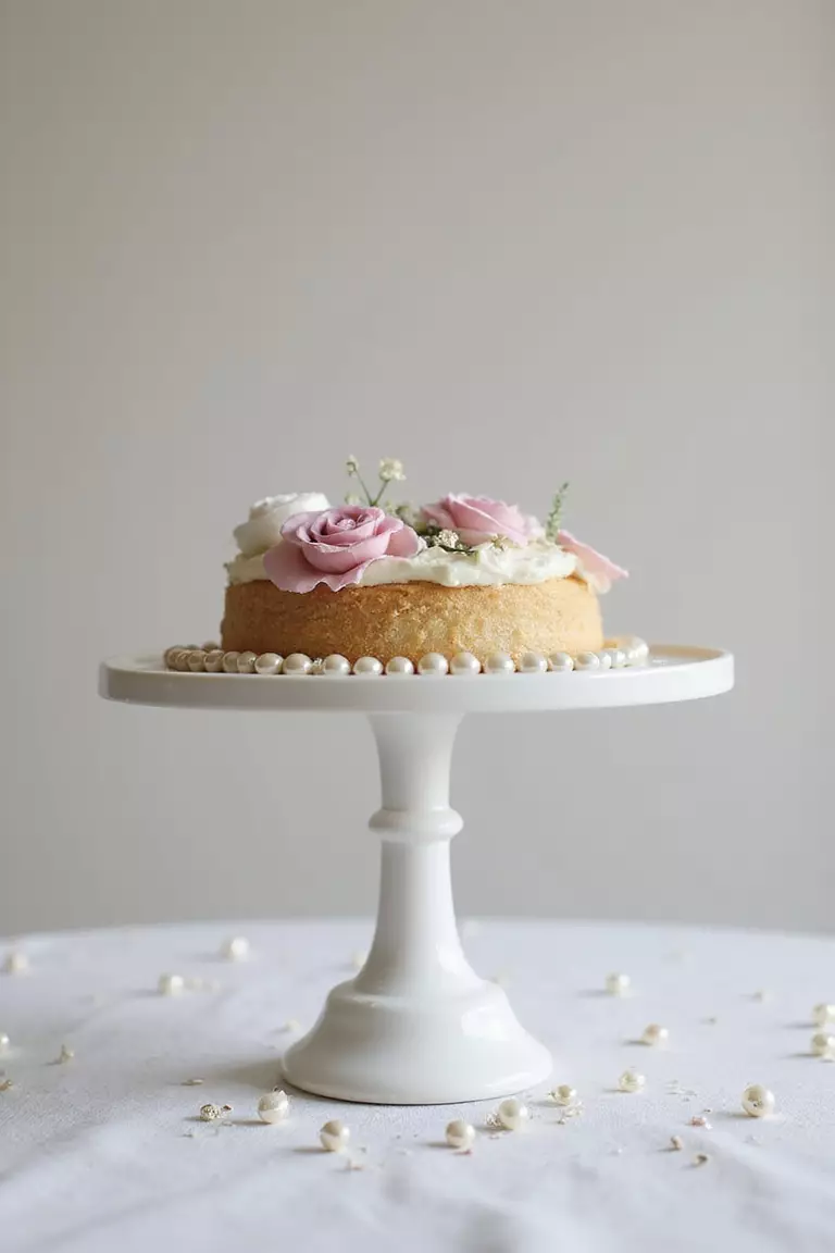 Cake Stand Creation A professional photo, similar to a photo in a wedding magazine, of a white ceramic cake stand displaying not a cake, but a small floral arrangement and scattered pearls.