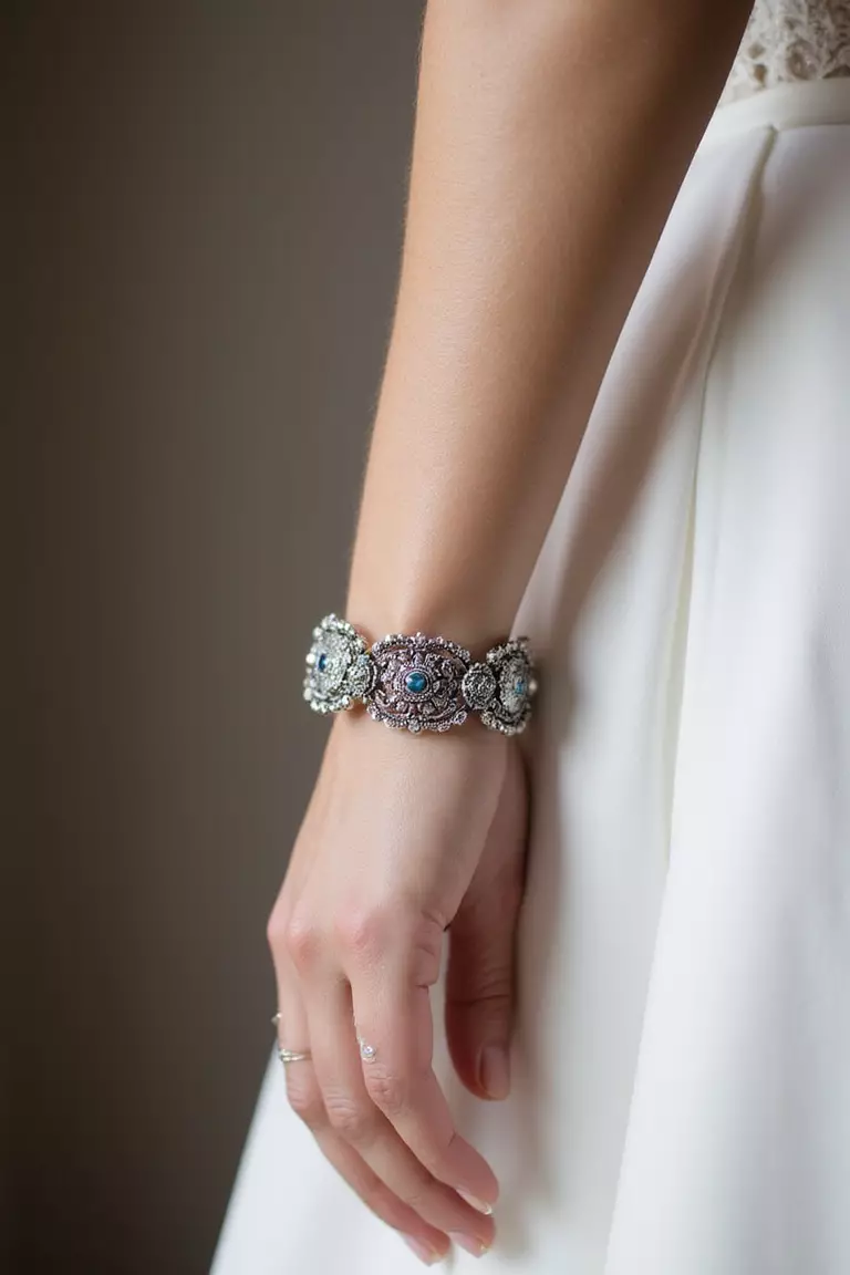 Heirloom Jewelry A professional photo, similar to a photo in a wedding magazine, of a close-up on a bride's wrist wearing an antique silver bracelet with intricate filigree details.