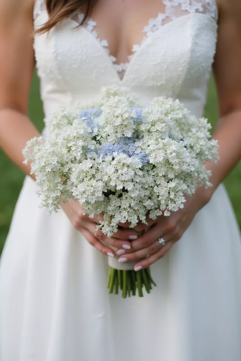 Queen Anne's Lace Cloud A professional photo, similar to a photo in a wedding magazine, of a bride holding an ethereal, mostly white bouquet of Queen Anne's lace with accents of pale blue nigella.