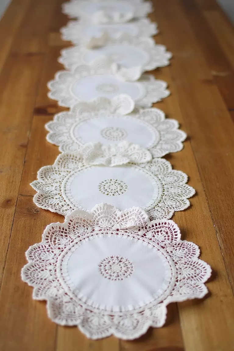 Doilies And Linens A professional photo, similar to a photo in a wedding magazine, of a wooden reception table runner made of delicate white lace doilies joined together.