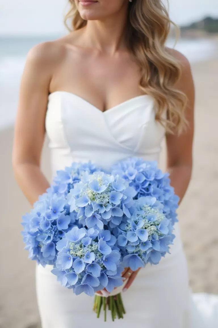 Hydrangea Hues A professional photo, similar to a photo in a wedding magazine, of a bride holding a full bouquet dominated by large blue and white hydrangea blooms, round and lush. Coastal setting background.