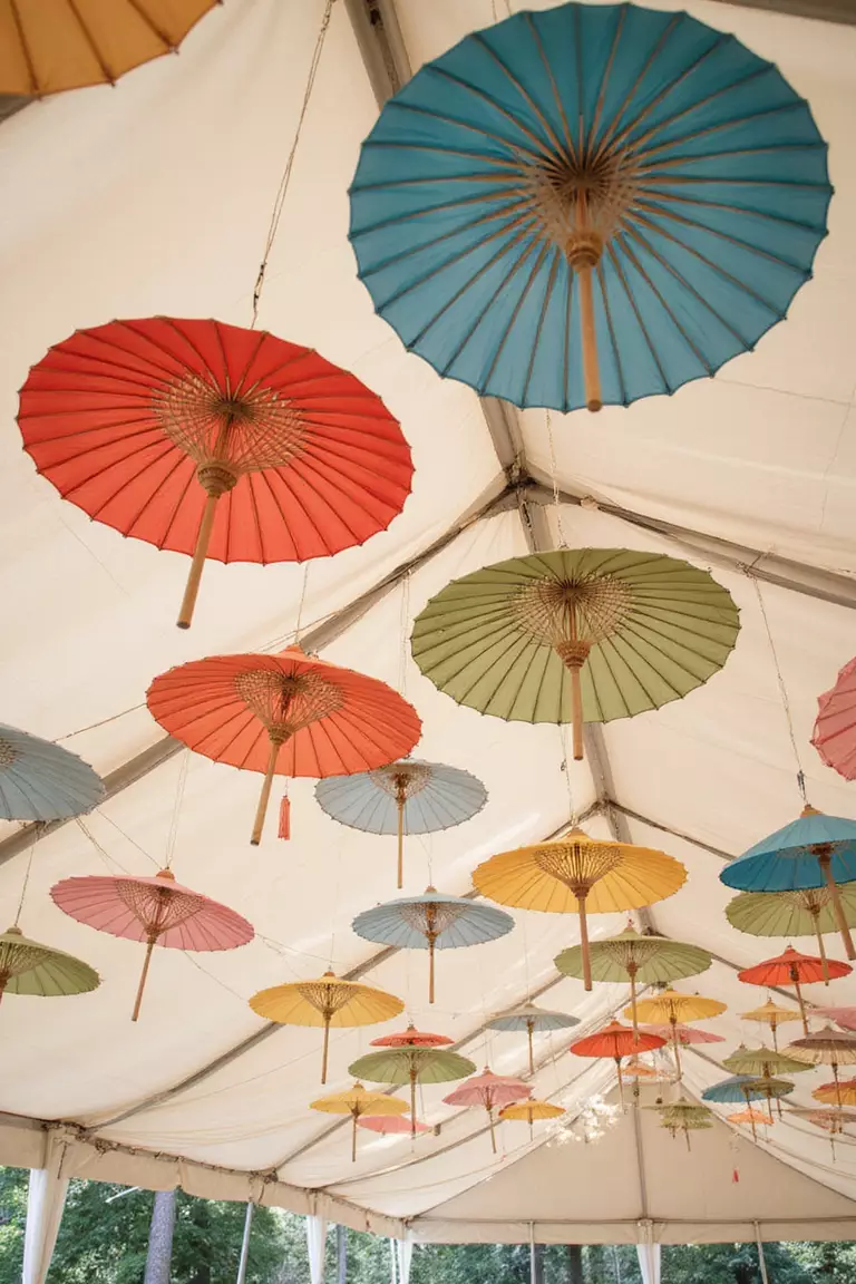 Parasol Accents A professional photo, similar to a photo in a wedding magazine, of colorful paper parasols hanging upside down from the ceiling of a wedding tent, casting soft light.