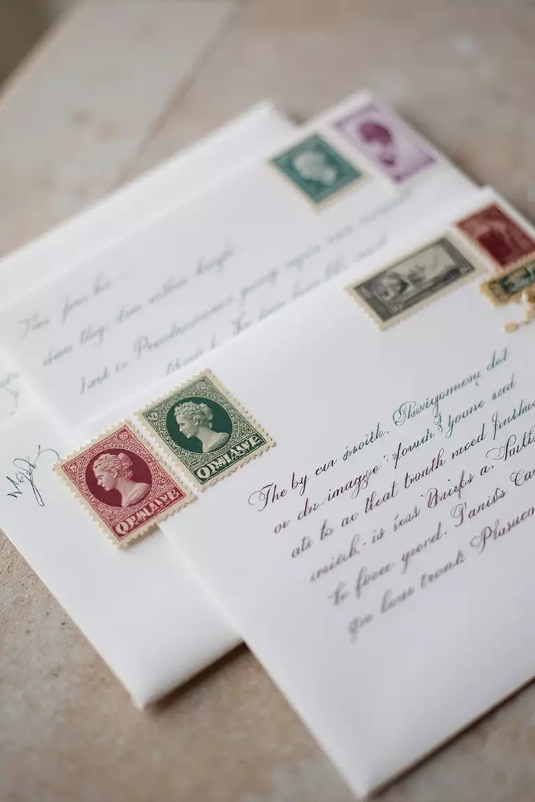 Vintage Stamps A professional photo, similar to a photo in a wedding magazine, of a close-up on wedding invitation envelopes adorned with various cancelled vintage postage stamps.