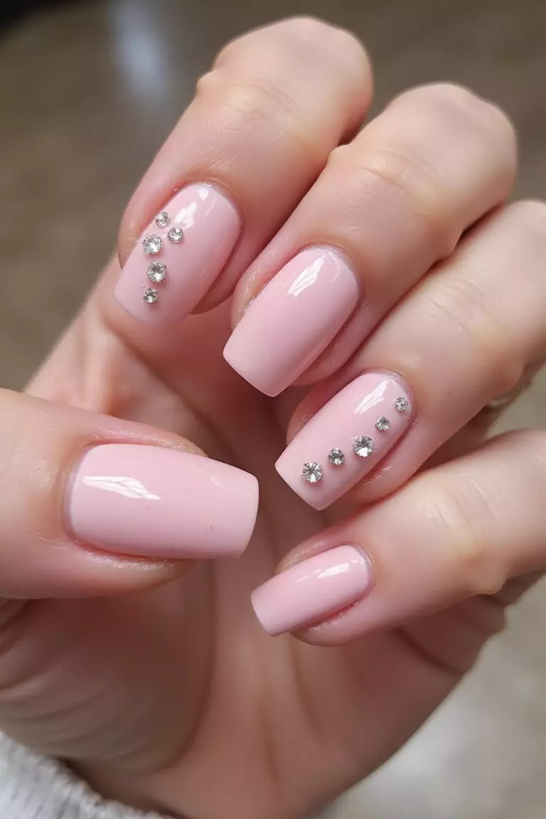 Pink Rhinestone Details Close-up of a woman's hand with five fingers featuring pink nails with tiny rhinestones placed along cuticles, forming delicate patterns.