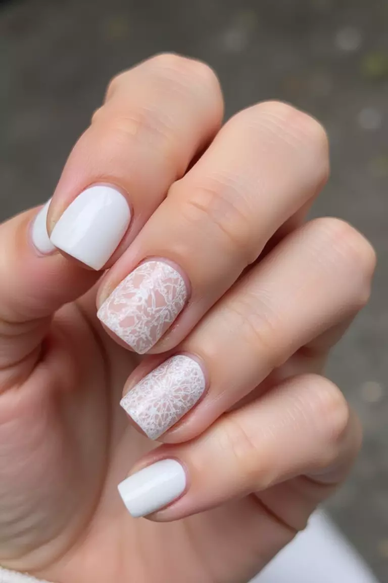 An Accent Pattern Close-up of a woman's hand with five fingers featuring white nails with one or two accent nails featuring detailed patterns in white-on-white designs.