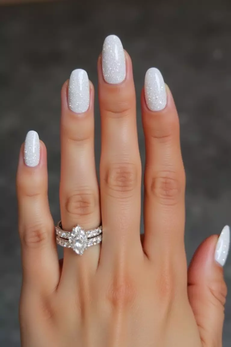 A Bedazzled Ring Finger Close-up of a woman's hand with five fingers featuring white nails with the ring finger covered in small, sparkling rhinestones catching the light.