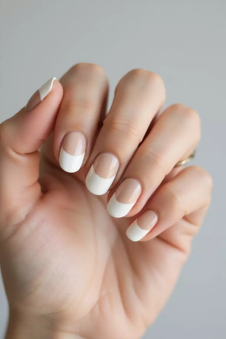 Close-up of a woman's hand showing nails transitioning from beige to white in a subtle gradient, photographed in soft light against simple background to highlight the smooth color blend.