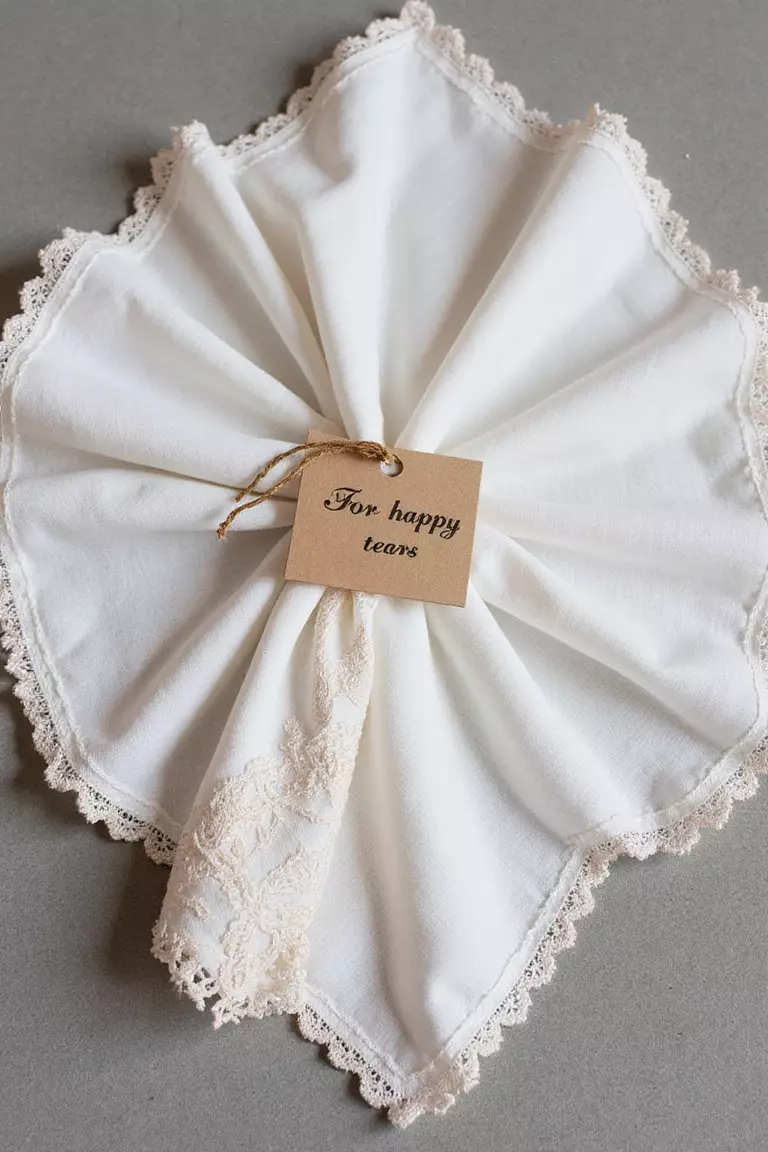 Vintage Handkerchiefs A professional photo, similar to a photo in a wedding magazine, of delicate vintage handkerchiefs with lace edges and embroidered details, folded neatly with a tag reading "For happy tears".