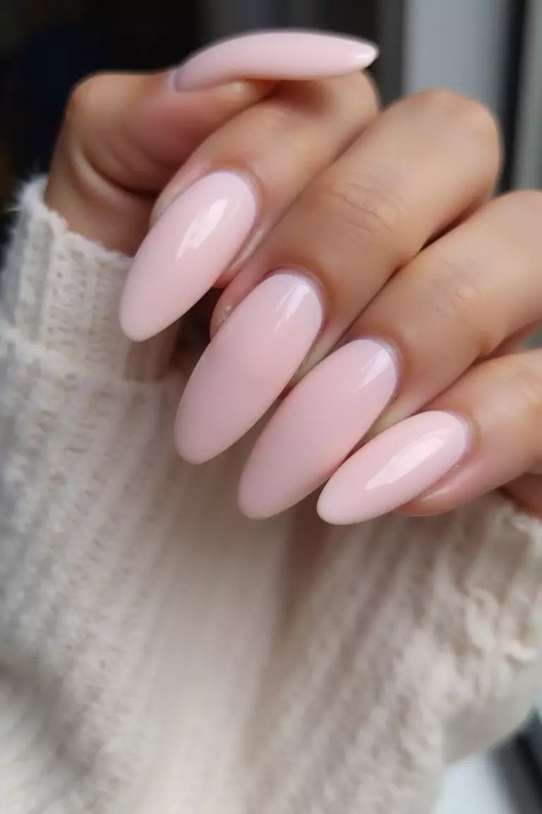 Ballerina Pink Almond Nails Close-up of a woman's hand with five fingers featuring pale pink almond-shaped nails, elongated and tapered, ballerina-inspired.