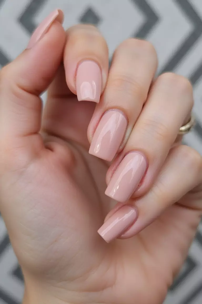 Square Shape Sophistication: Geometric Appeal for Summer Brides Close-up of a woman's hand with perfectly squared nails in a pale blush color with precise edges and subtle shimmer against a geometric patterned background.