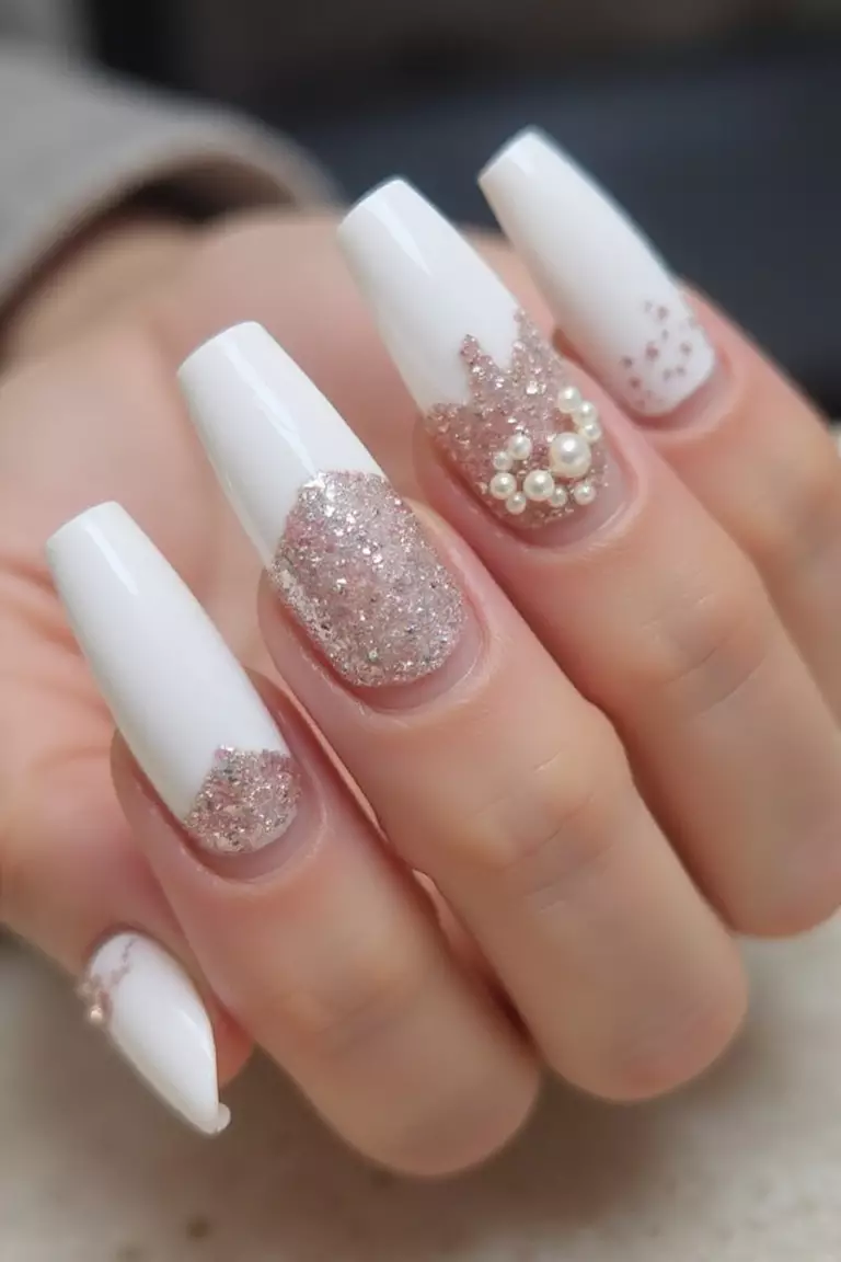 A Mix & Match Mani Close-up of a woman's hand with five fingers featuring white nails with each nail sporting a different design, including glitter, pearls, and minimalist patterns.