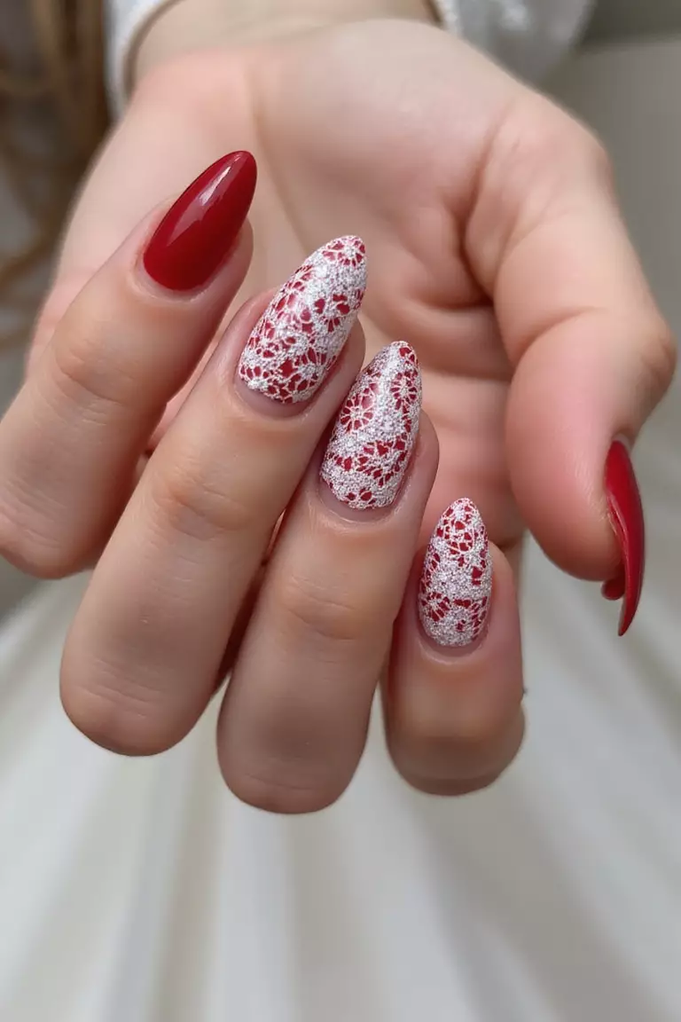 Close-up of a woman's hand with elegant red nails featuring delicate white lace patterns, mimicking wedding dress details, against a neutral background.