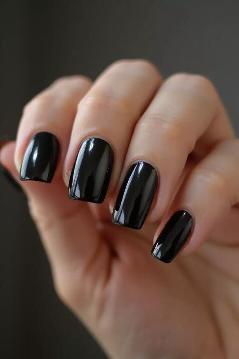 Black Chrome Nails Close-up of a woman's hand with five fingers featuring black chrome nails with mirror-like metallic finish reflecting light dramatically.