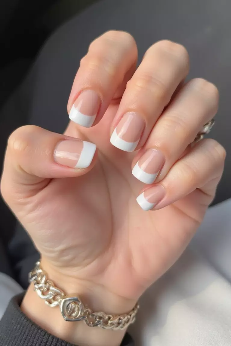 Ombre Tips Close-up of a woman's hand with five fingers featuring short nails with a subtle gradient ombre effect from nude at the base to white at the tips.