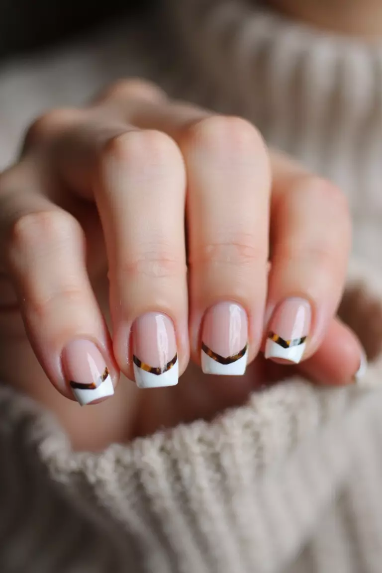 French Tortoise Close-up of a woman's hand with five fingers featuring short nails with a modern French manicure using tortoiseshell pattern on the tips instead of white.