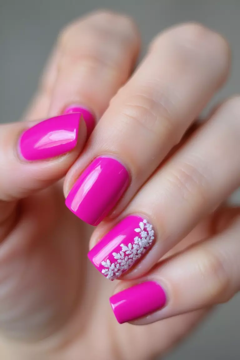 Hot Pink Passion: Bold and Vibrant Statements Close-up of a woman's hand with vibrant hot pink nails featuring a glossy finish, slight shimmer, and delicate white accent designs on the ring finger against a neutral background.