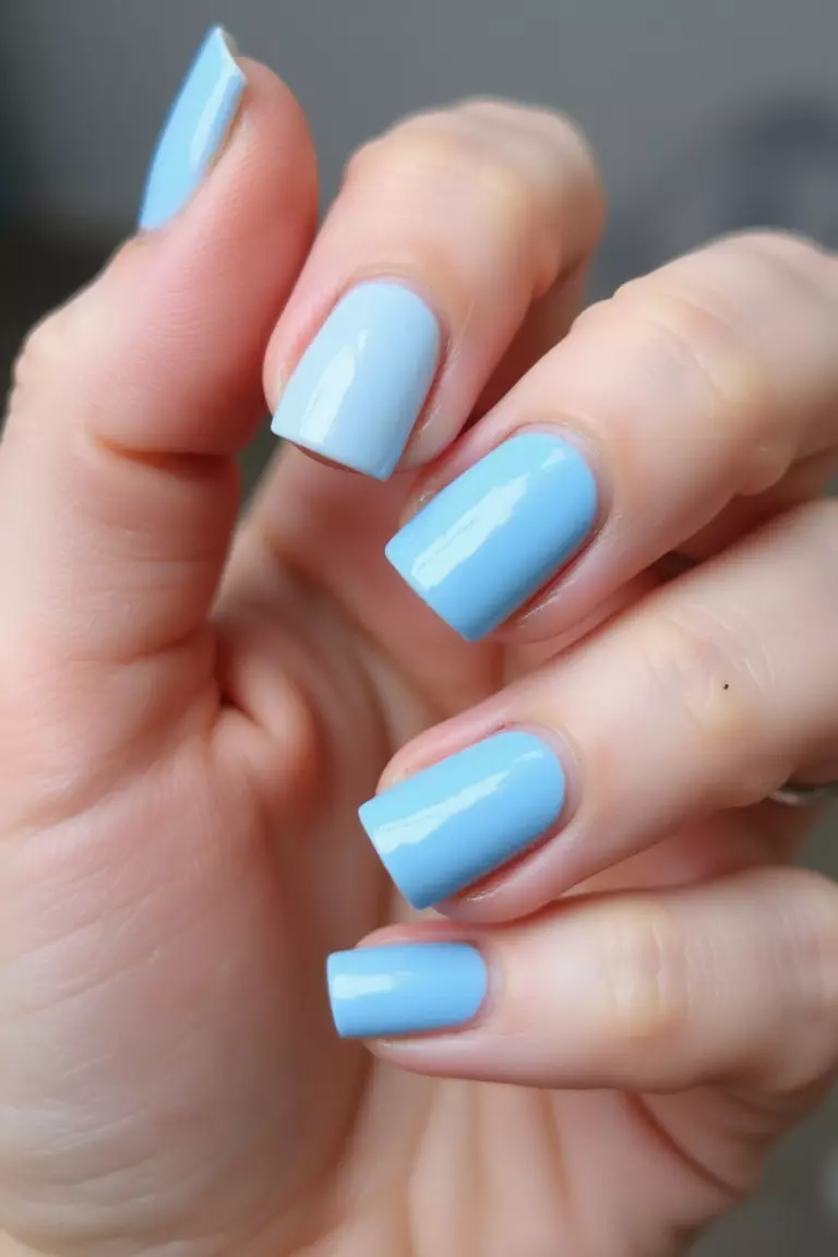 Something Blue Close-up of a woman's hand with five fingers featuring short nails in various light blue shades, from powder blue to periwinkle, with a glossy finish.
