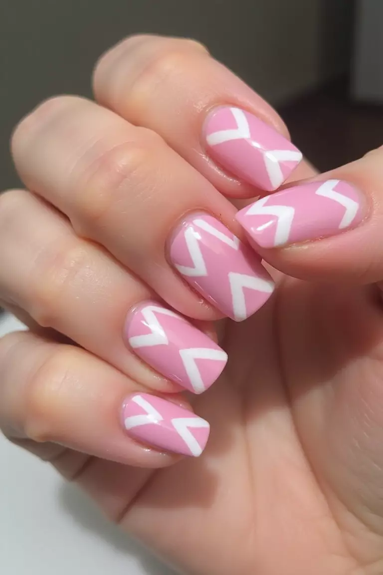 Pink Chevron Design Close-up of a woman's hand with five fingers featuring pink nails with white chevron patterns, geometric V-shaped designs.