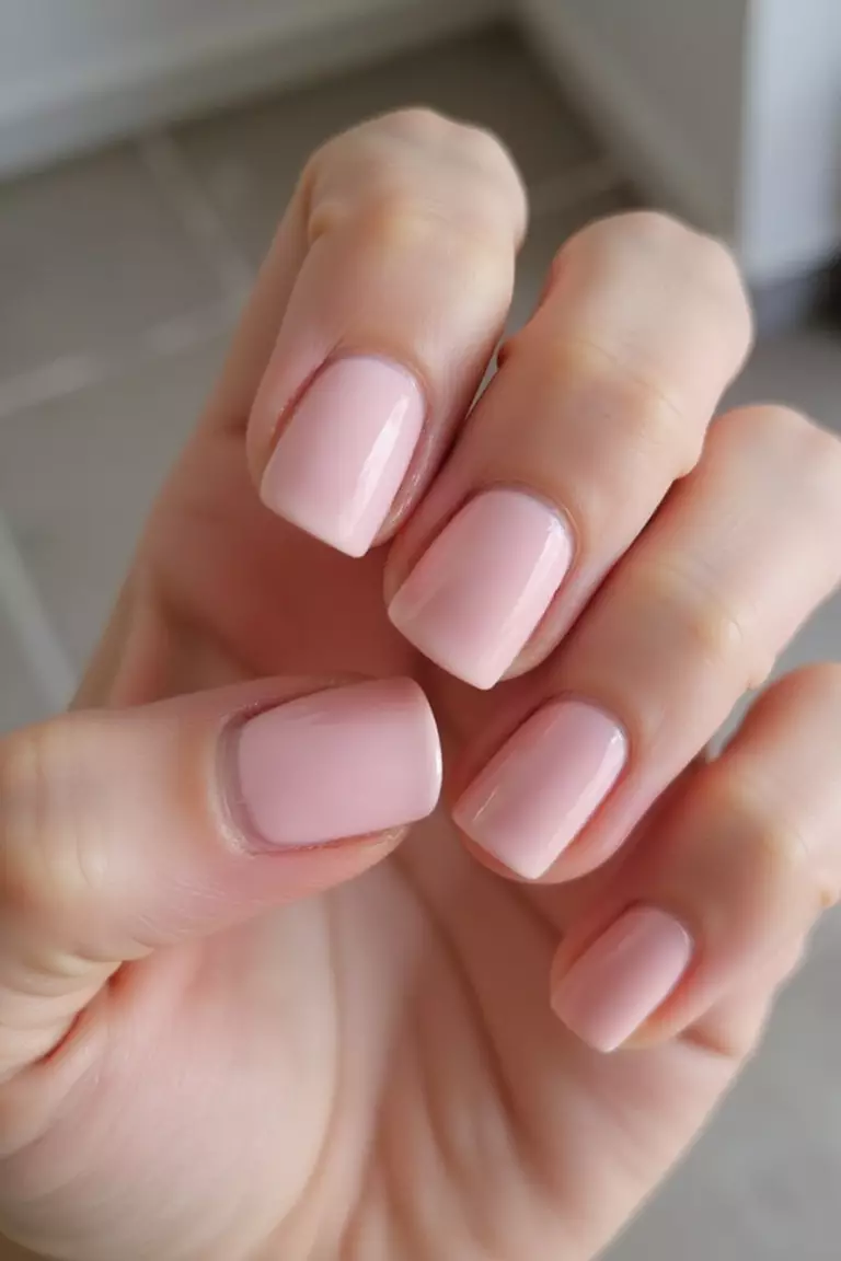 Baby Pink Close-up of a woman's hand with five fingers featuring short nails painted in soft baby pink with a smooth finish, showing a delicate feminine manicure.