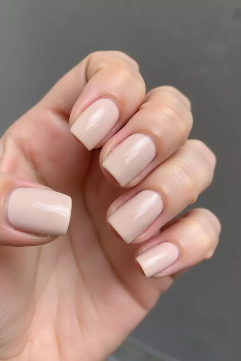 Close-up of a woman's hand showing clean square-shaped nails with glossy neutral polish, photographed in natural light against simple background to highlight the precise shape.