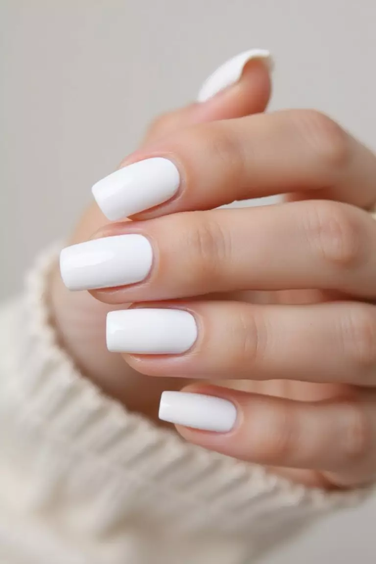 Elegant Simplicity: Classic White Bridal Nails Close-up of a woman's hand with pure white nails in a glossy finish, perfectly shaped with clean edges against a soft, light background.