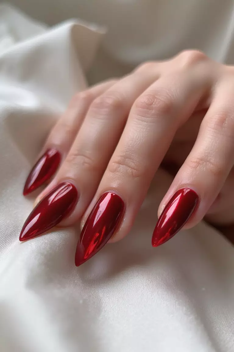Close-up of a woman's hand with mirror-like red chrome nails reflecting light beautifully, creating a metallic sheen, posed against white satin.