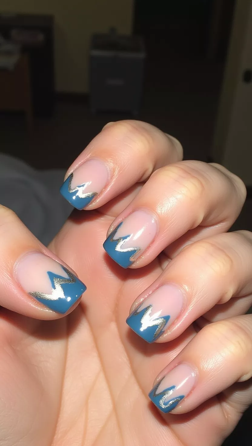 Swirly French close-up shot of a woman’s hand with five fingers showing nails with a clear base and thin, wavy lines of medium blue and silver polish flowing irregularly across the tips of the nails, room background