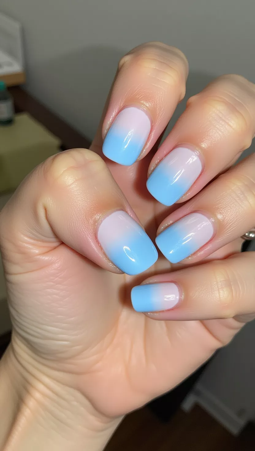 Aura Nails close-up shot of a woman’s hand with five fingers showing nails with a soft, gradient circular design of bright electric blue concentrated in the center, blending outward to a milky pale blue edge, room background