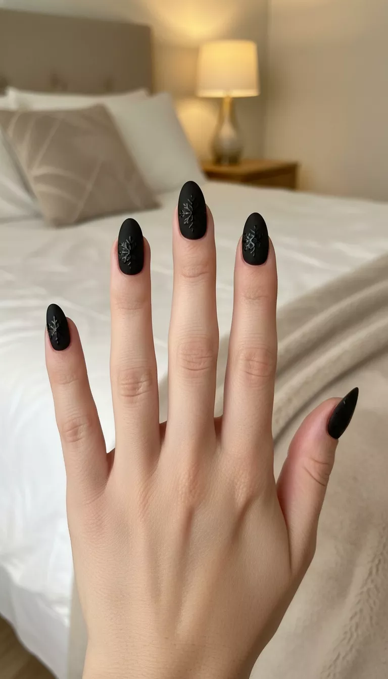 close-up shot of a woman’s hand with five fingers showing nails with a flat matte black polish with small, intricately hand painted glossy black snowflakes on every nail, bedroom background.