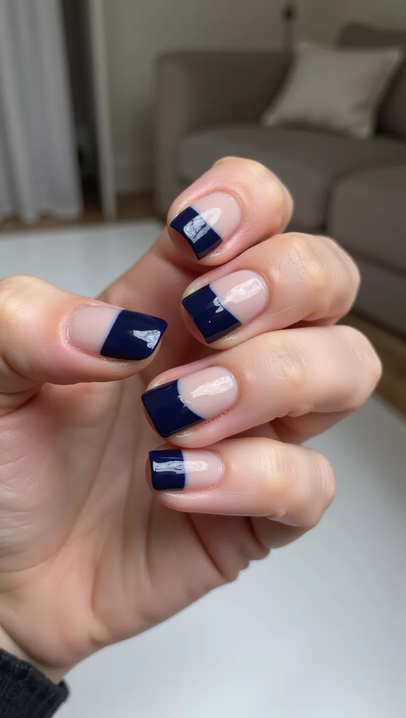 Midnight Blue French close-up shot of a woman’s hand with five fingers showing nails with a sheer, cool-toned nude base and deep, opaque midnight blue French tips, room background