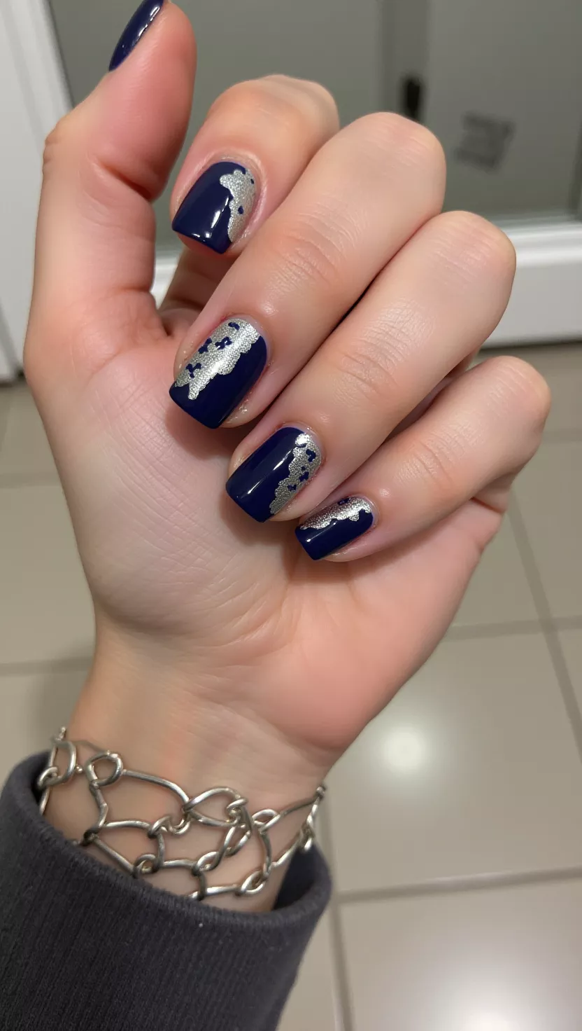 Navy & Silver close-up shot of a woman’s hand with five fingers showing nails with a navy blue base color and silver foil accents irregularly placed, room background