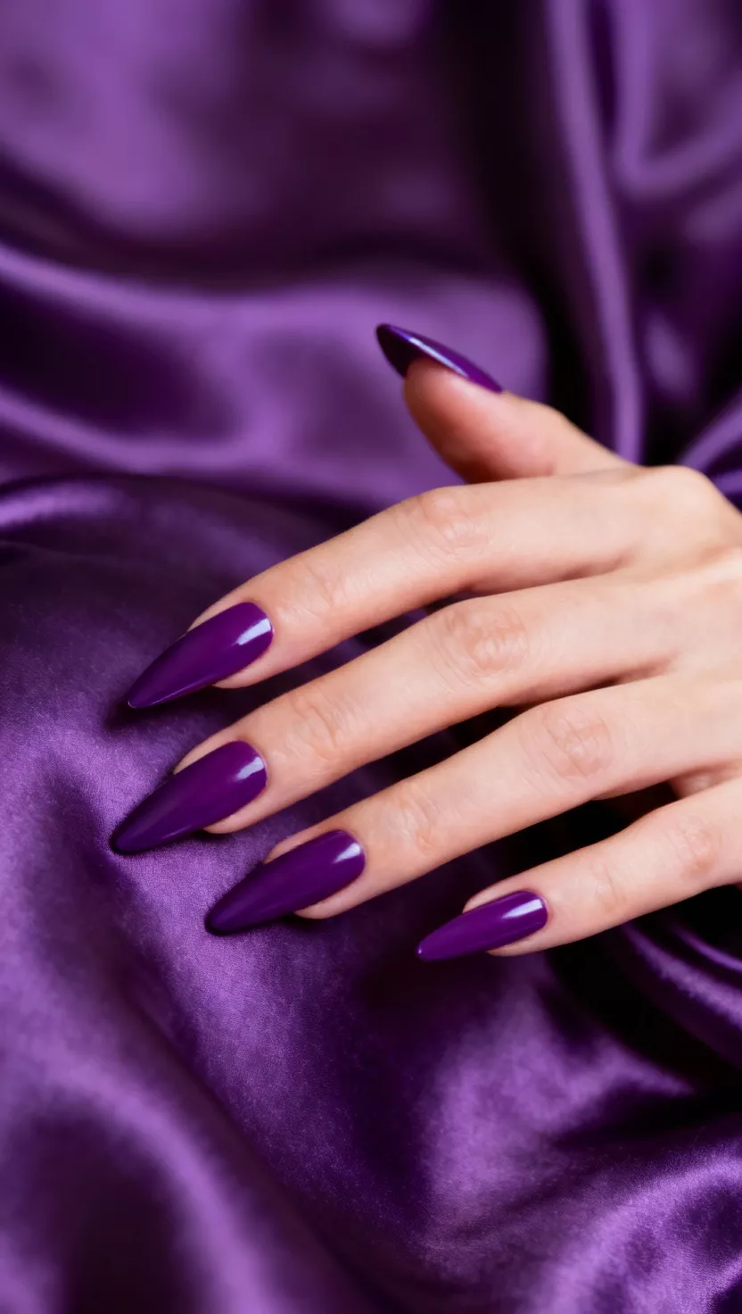close-up shot of a woman’s hand with five fingers showing stiletto shaped nails with a saturated, deep purple cream polish, silk fabric background.