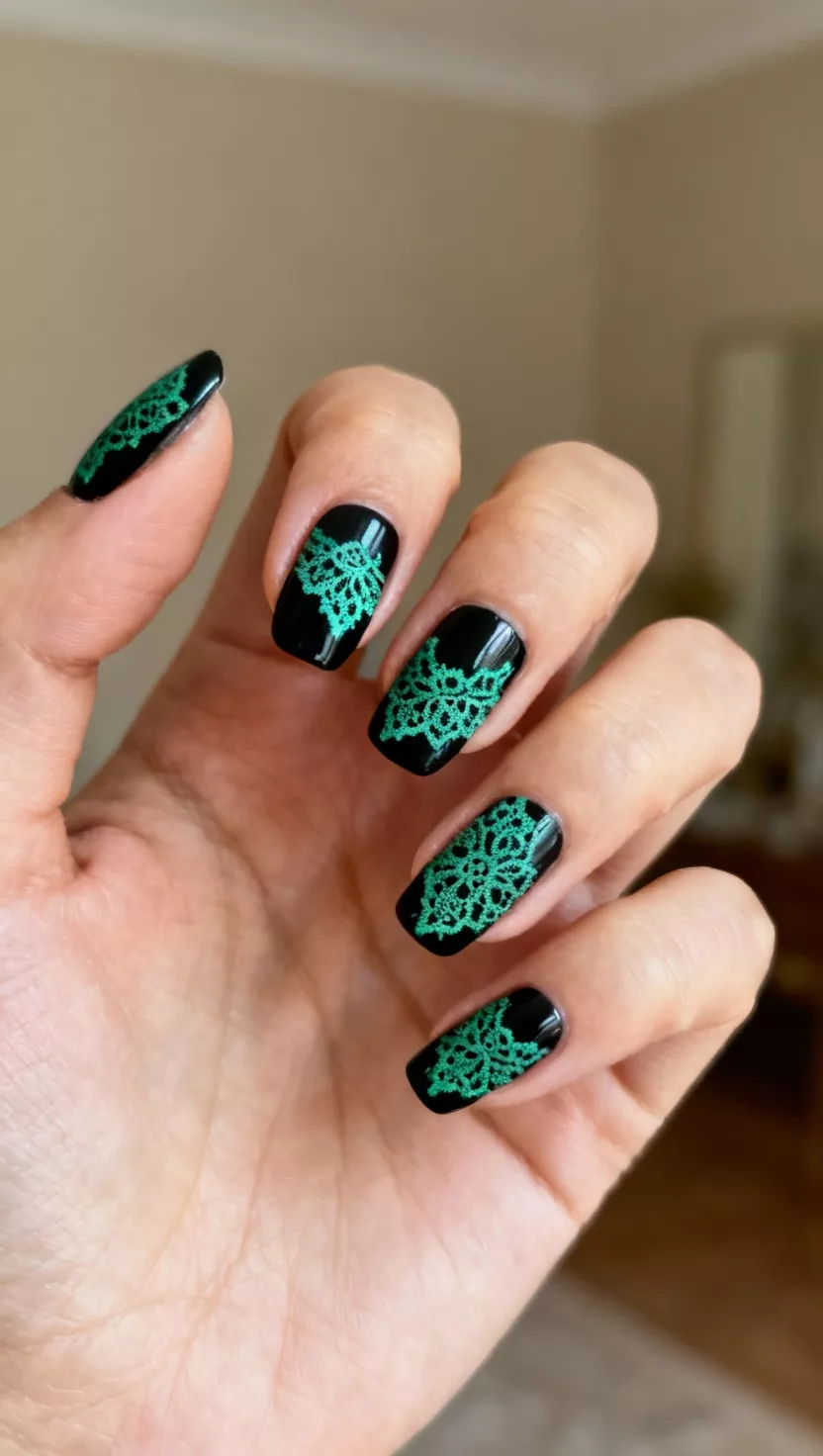 close-up shot of a woman’s hand with five fingers showing nails with an opaque black base and intricate emerald green stamping art featuring delicate lace patterns, room background.