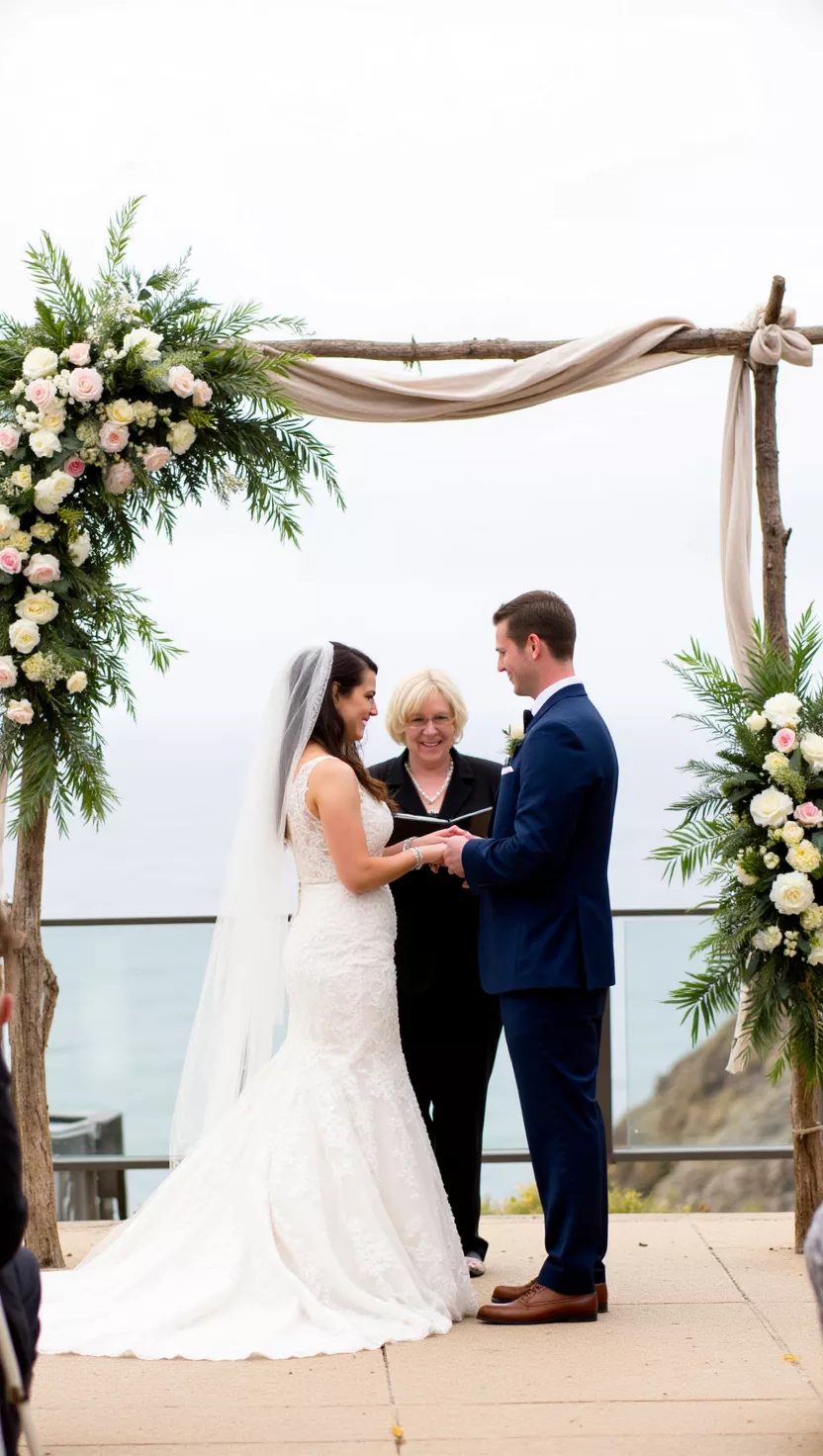 Ocean Vow Exchange A photo of a bride and groom exchanging vows during an outdoor ocean view wedding ceremony, perfectly framed by dramatic and abundant floral arrangements.