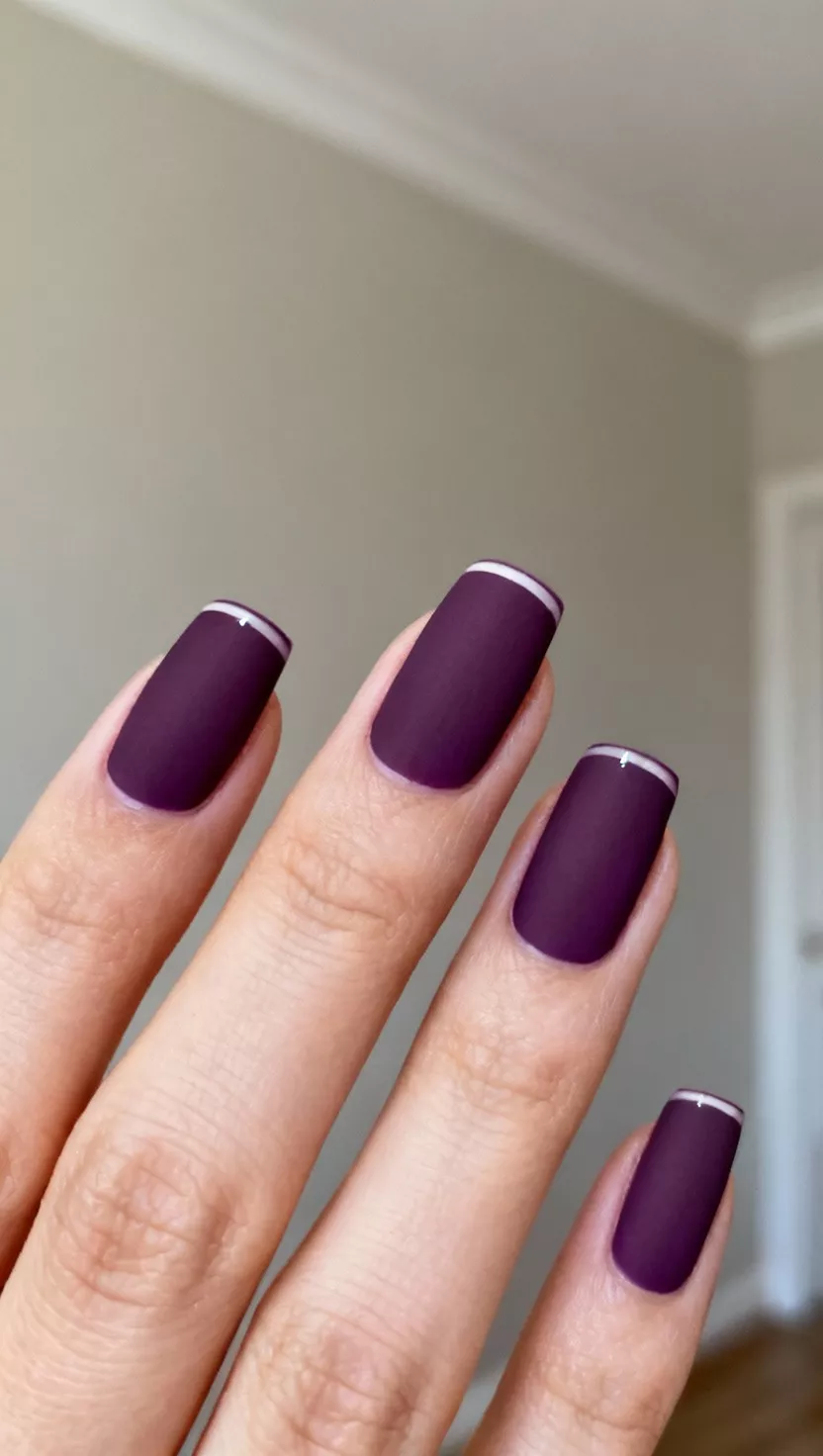 close-up shot of a woman’s hand with five fingers showing nails with a dark eggplant purple color with a matte finish, featuring a perfect, thin glossy French tip edge, neutral painted wall room background.