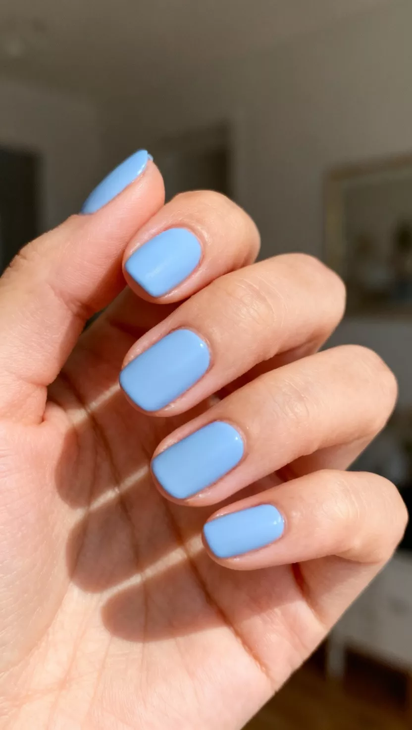 Periwinkle Blue Perfection close-up shot of a woman’s hand with five fingers showing nails with a vibrant but soft periwinkle blue polish with an opaque creme finish, room background.