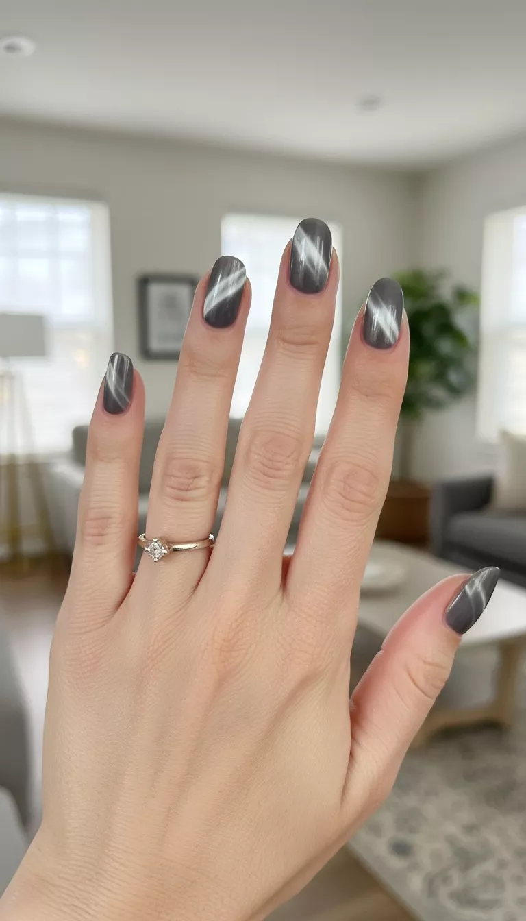 Smoky Gray Cat Eye close-up shot of a woman’s hand with five fingers showing nails with a sophisticated smoky gray magnetic polish, cured after using the magnet to create a mesmerizing diagonal line of light resembling a cat’s eye pupil, room background.