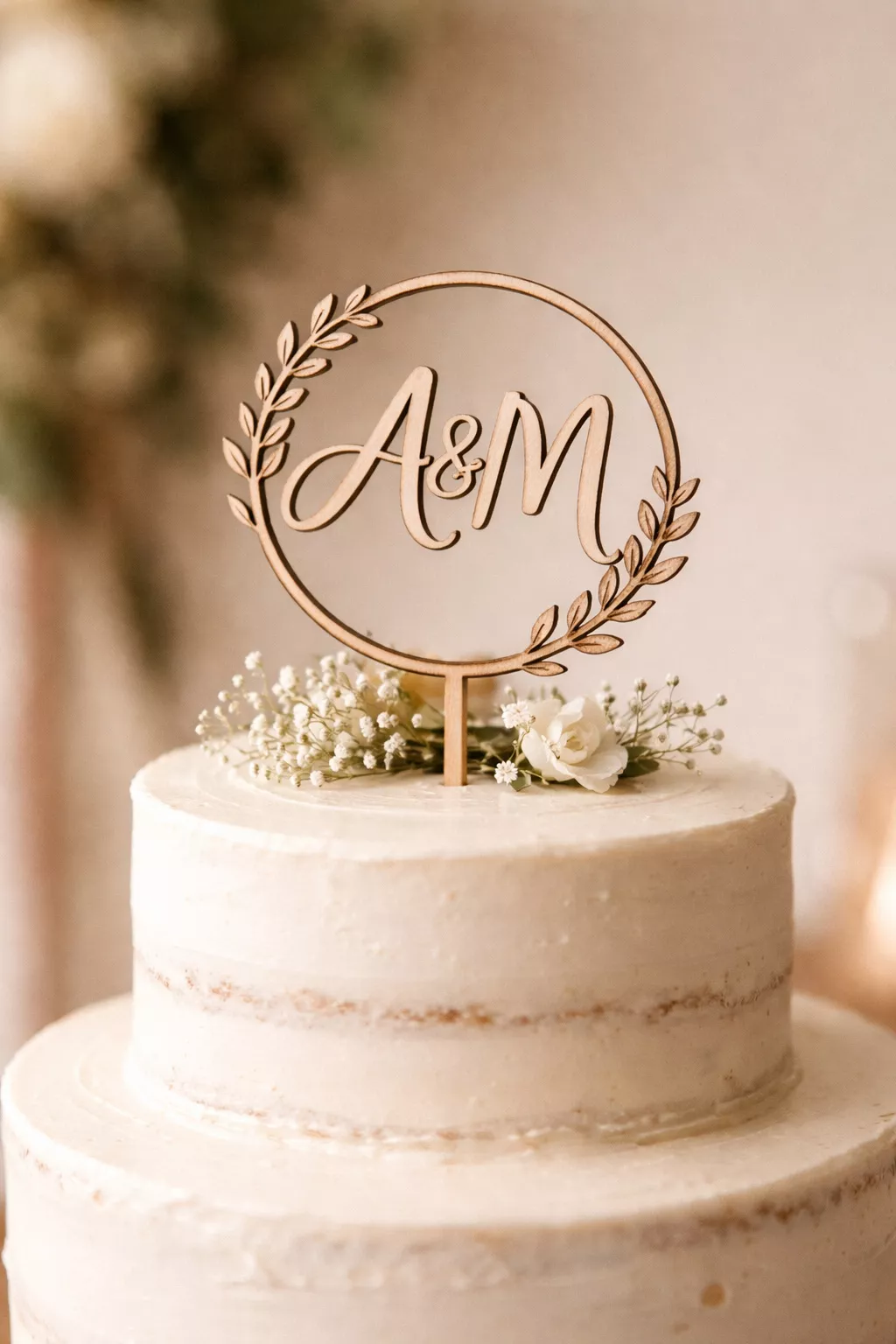 Personalized Cake Topper A realistic photo of a small wooden cake topper featuring laser-cut initials in a circle, resting on top of a simple white tiered cake with minimal frosting.