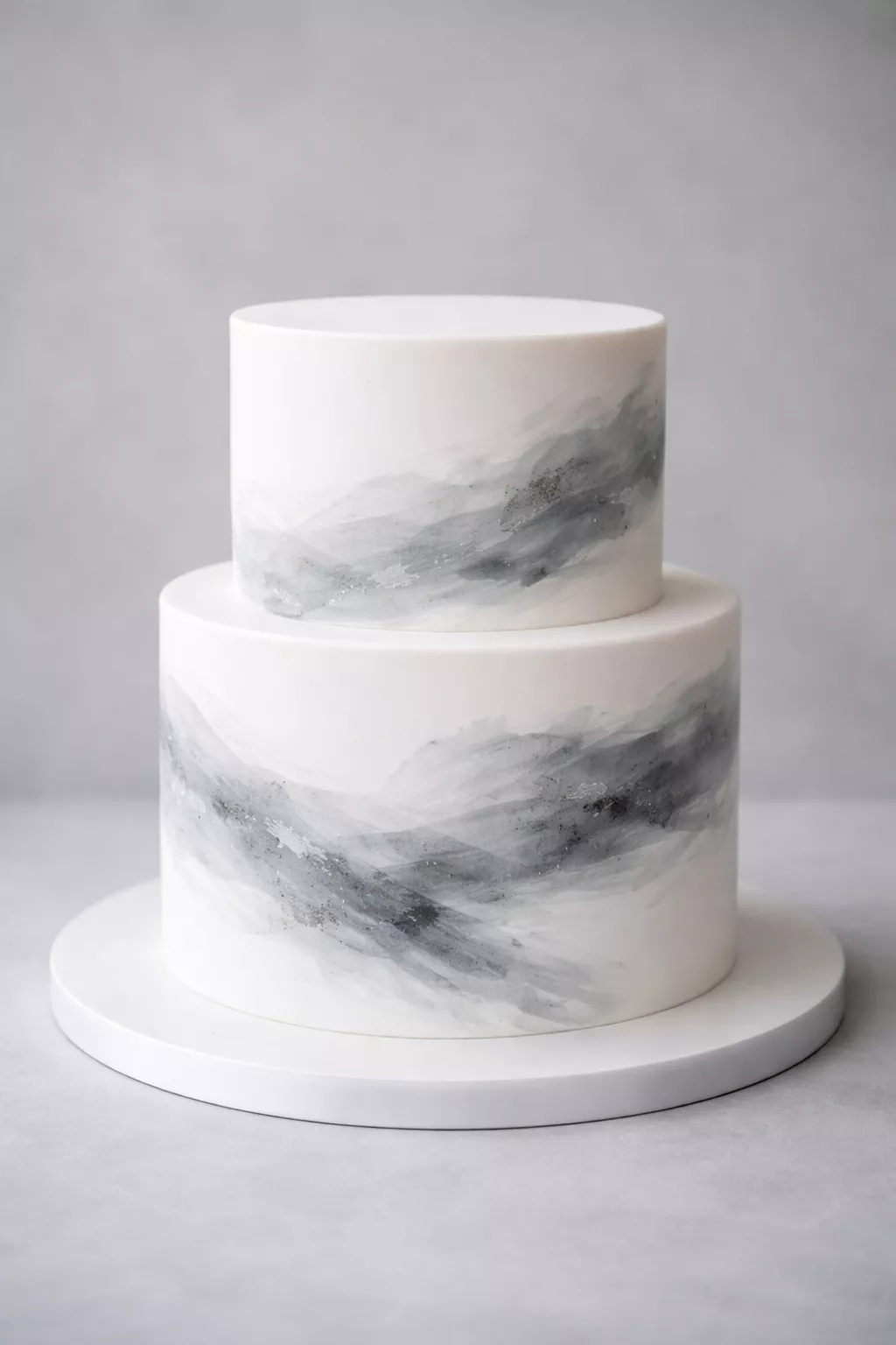 Tonal Brushstroke Cake A realistic photo of a two-tiered white wedding cake featuring subtle gray and charcoal edible brushstrokes that look like a watercolor painting, set against a monochromatic gray backdrop.
