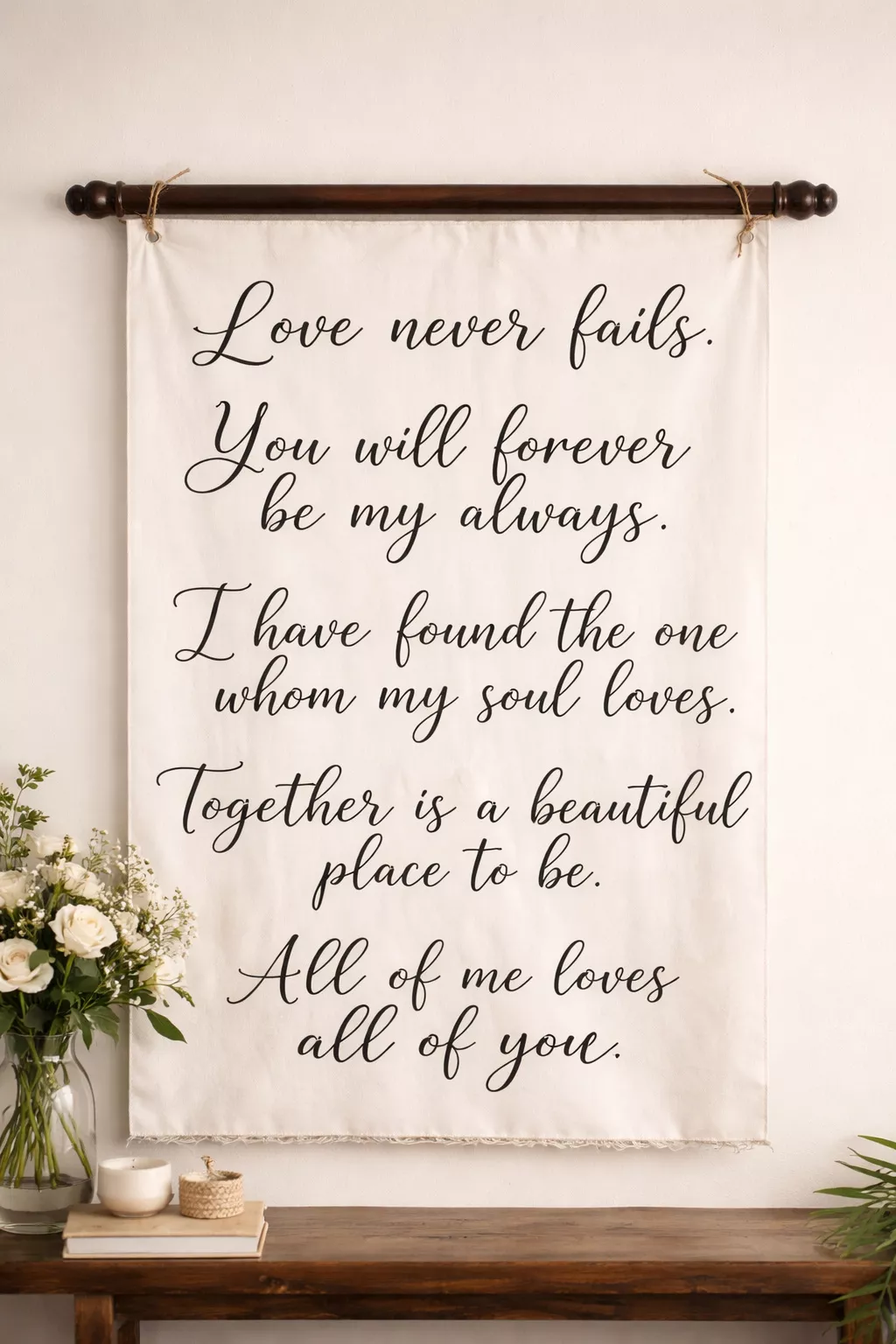 A realistic photo of a large white canvas banner with black cursive calligraphy love quotes hanging from a dark wooden rod.
