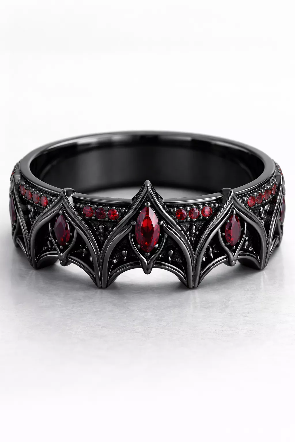 A realistic photo of a black gold wedding band with deep red rubies and a sharp gothic arch motif.